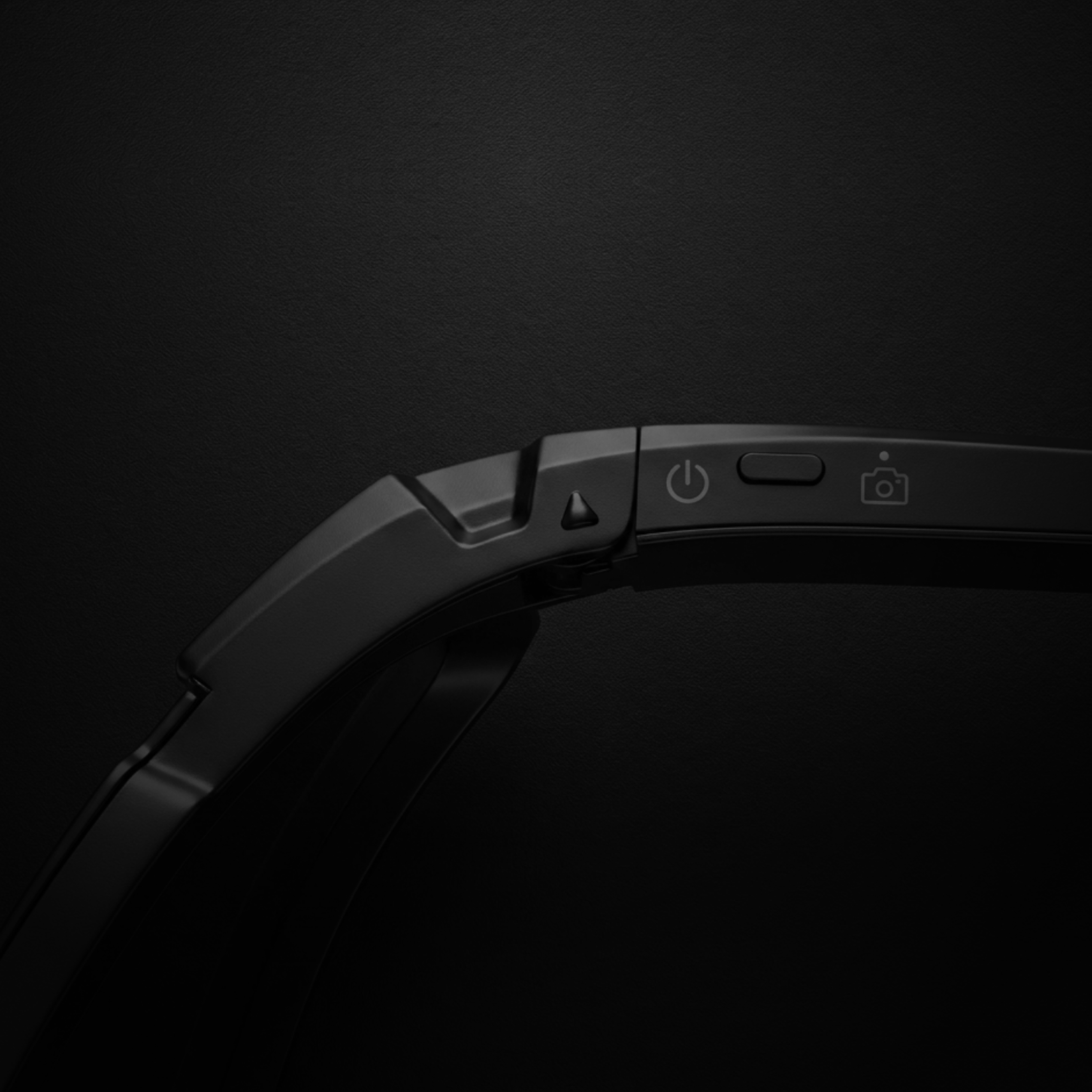 Close-up of AI sports glasses with camera showing power and camera buttons on a black background.