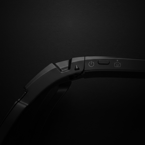 Close-up of AI sports glasses with camera showing power and camera buttons on a black background.